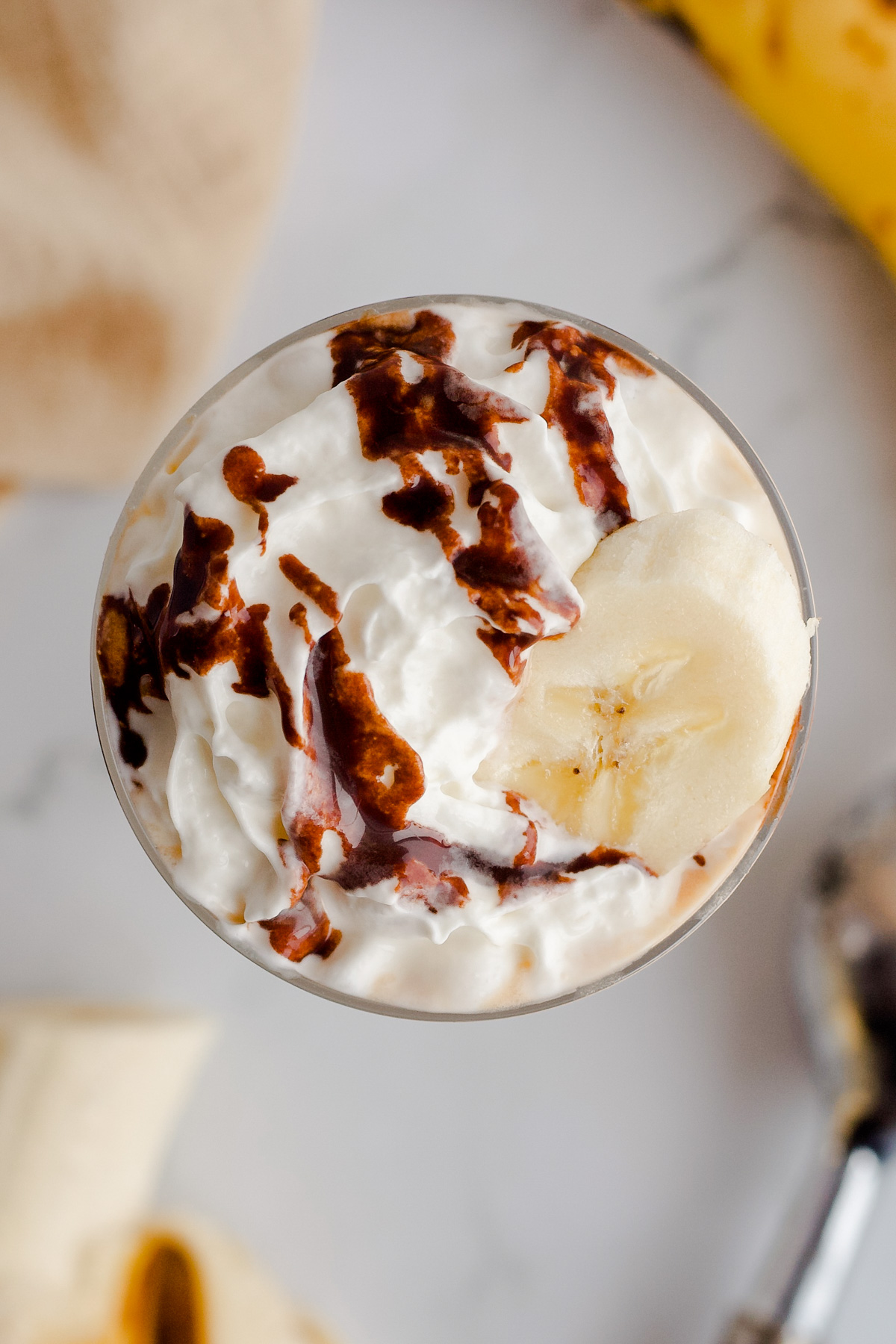 Overhead view of milkshake with whipped cream, chocolate syrup and banana slice