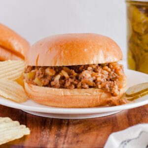 Sloppy Joe with chips and pickles served on white plate