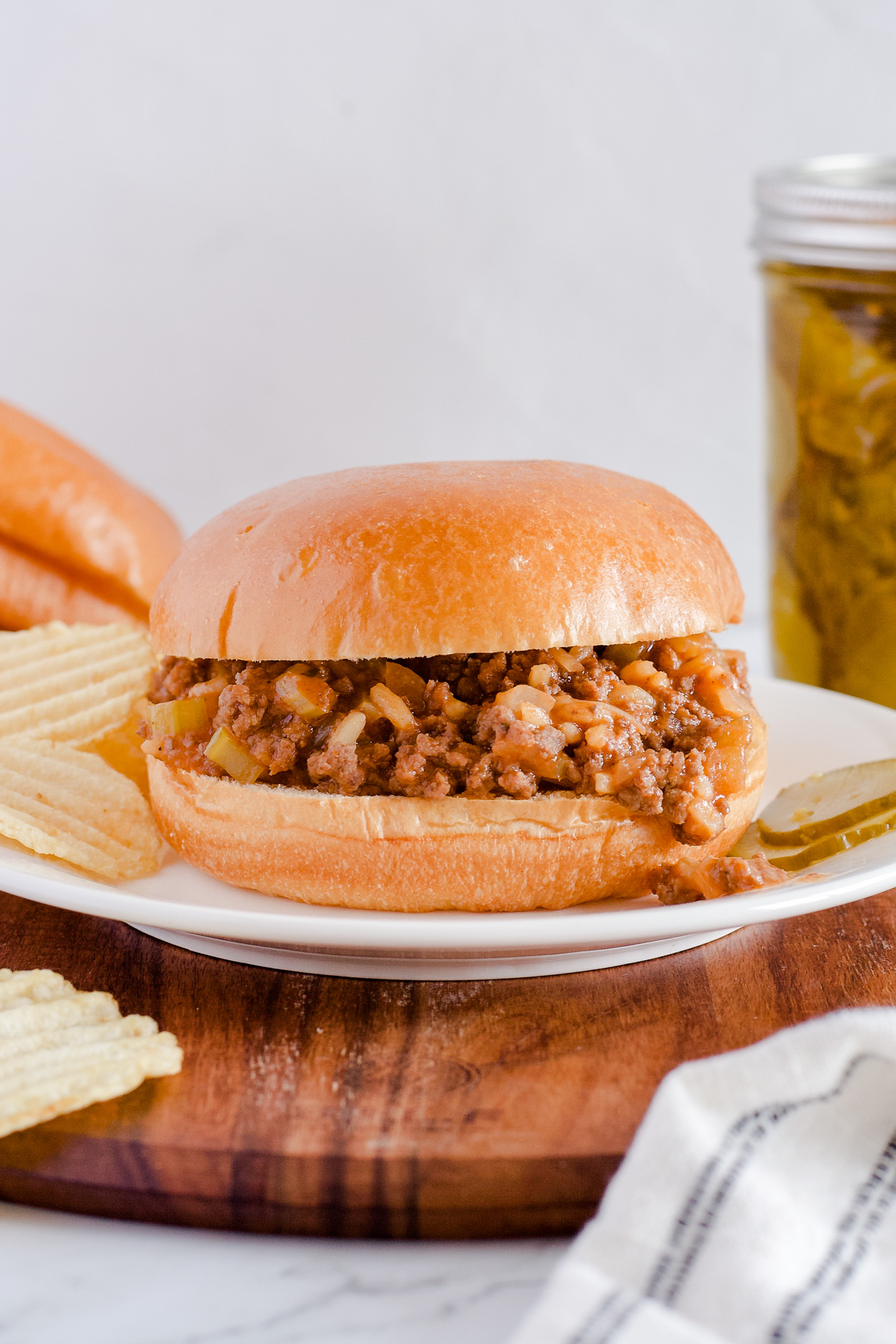 Sloppy Joe served with chips and pickles on a white plate