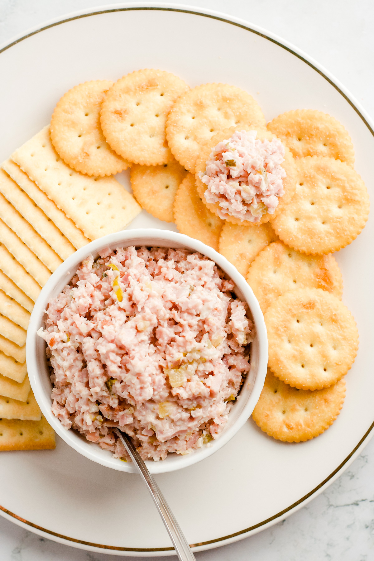 White bowl of ham salad on a white plate with rectangle and round crackers