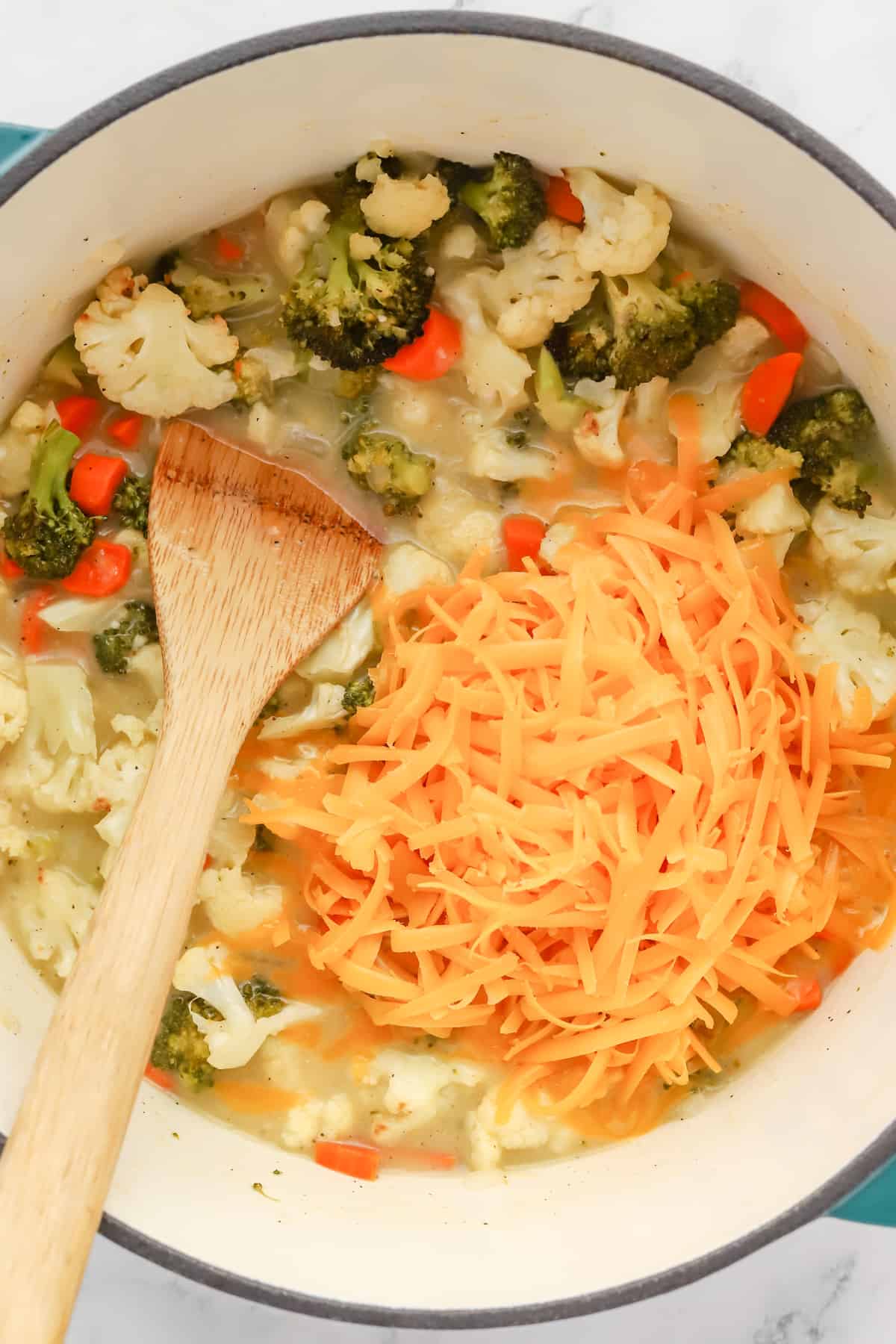Shredded cheddar cheese in pot with vegetables and soup base. 