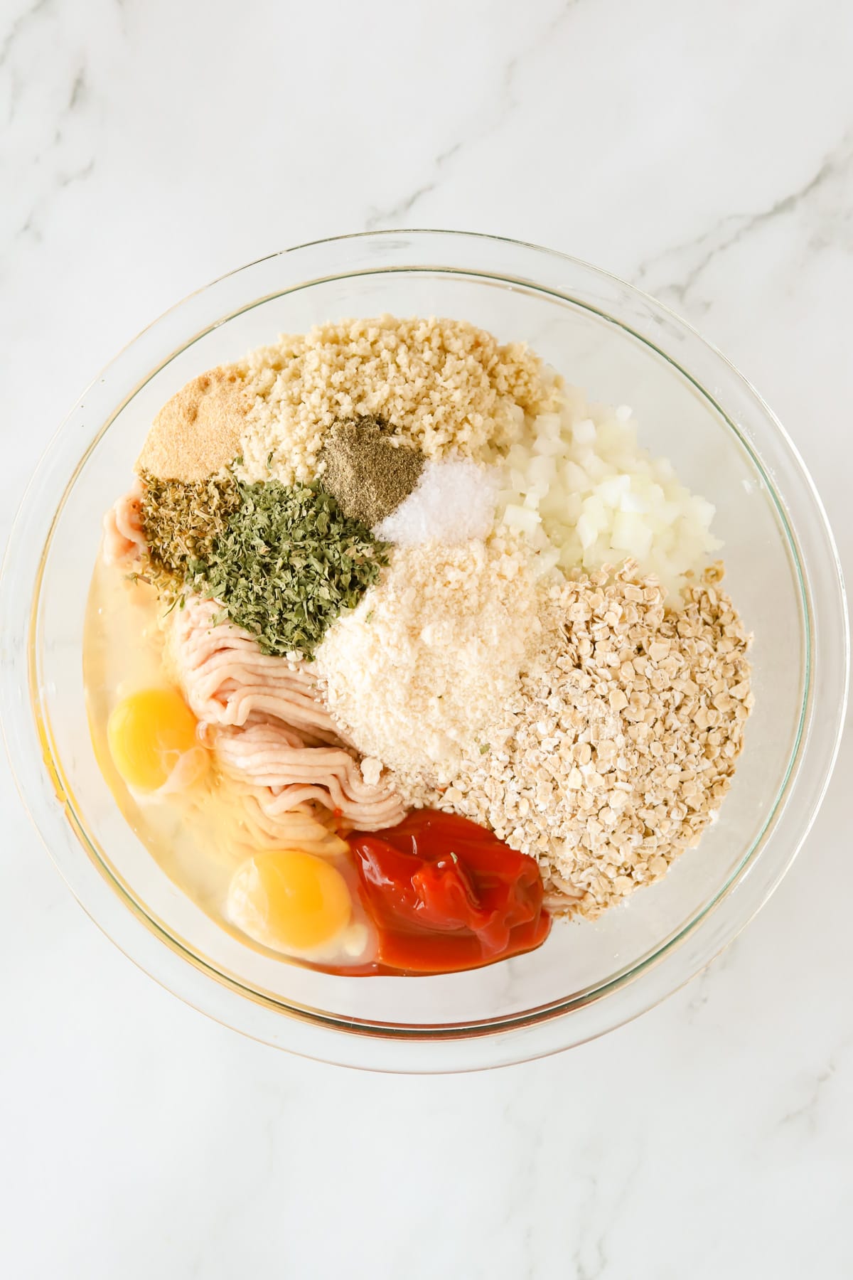 Overhead shot of meatloaf ingredients separated in a glass bowl