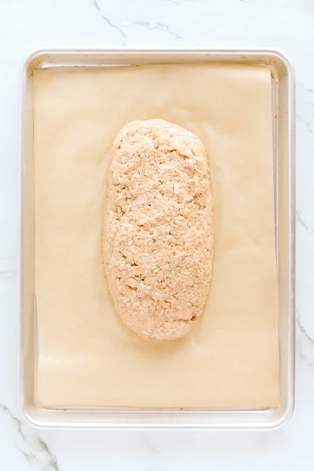 Raw meatloaf on a brown parchment lined metal baking sheet. Overhead shot.Raw meatloaf on a brown parchment lined metal baking sheet. Overhead shot.