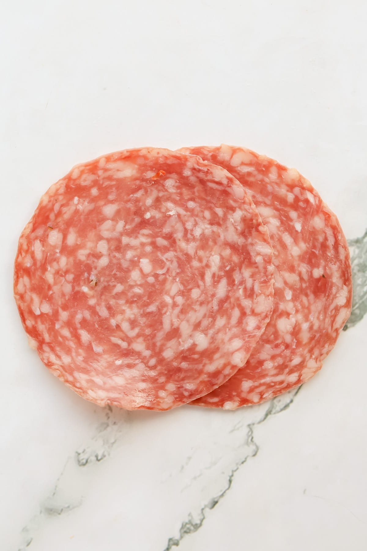 Two pieces of salami on countertop overlapping by an inch