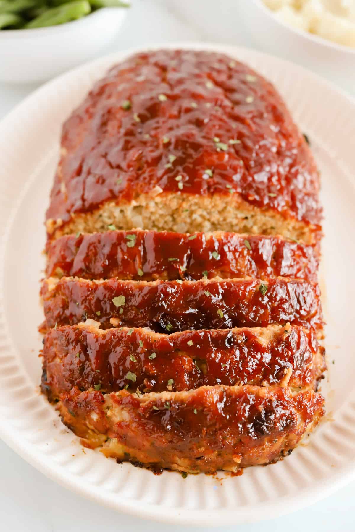 Angled view of chicken meatloaf on a white oval platter with four slices made. These slices are laying stacked on each other.