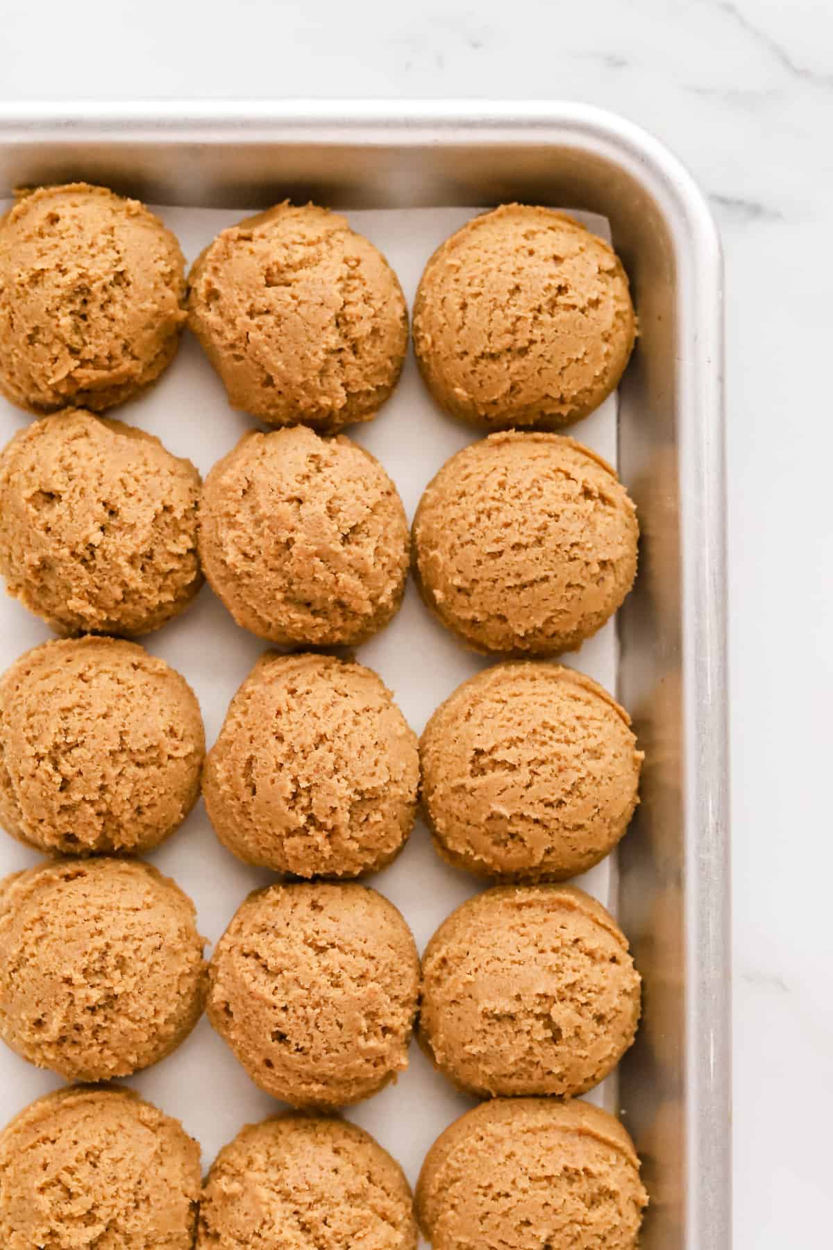 Cookie dough balls lined up on a parchment lined baking sheet ready to be chilled. 