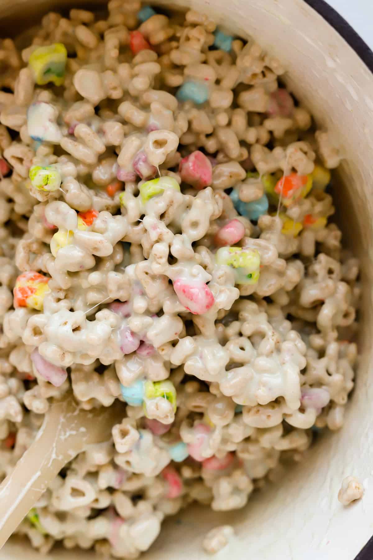 Rubber spatula mixing cereal into melted marshmallows and butter mixture in dutch oven.