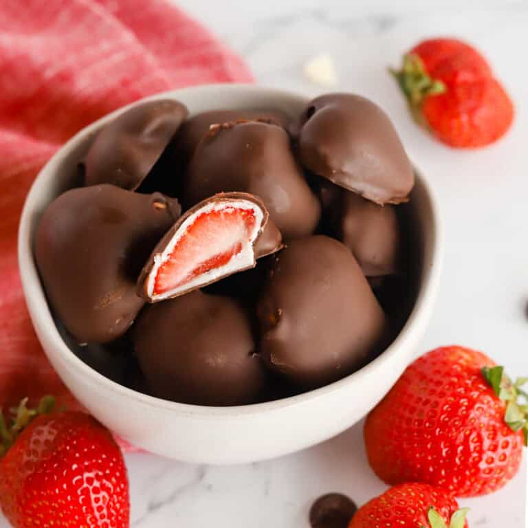 Small white bowl of dipped berries with one on top cut in half, exposing the center.
