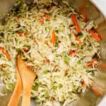 Overhead shot of large silver bowl of coleslaw with 2 wooden spoons resting in the slaw.
