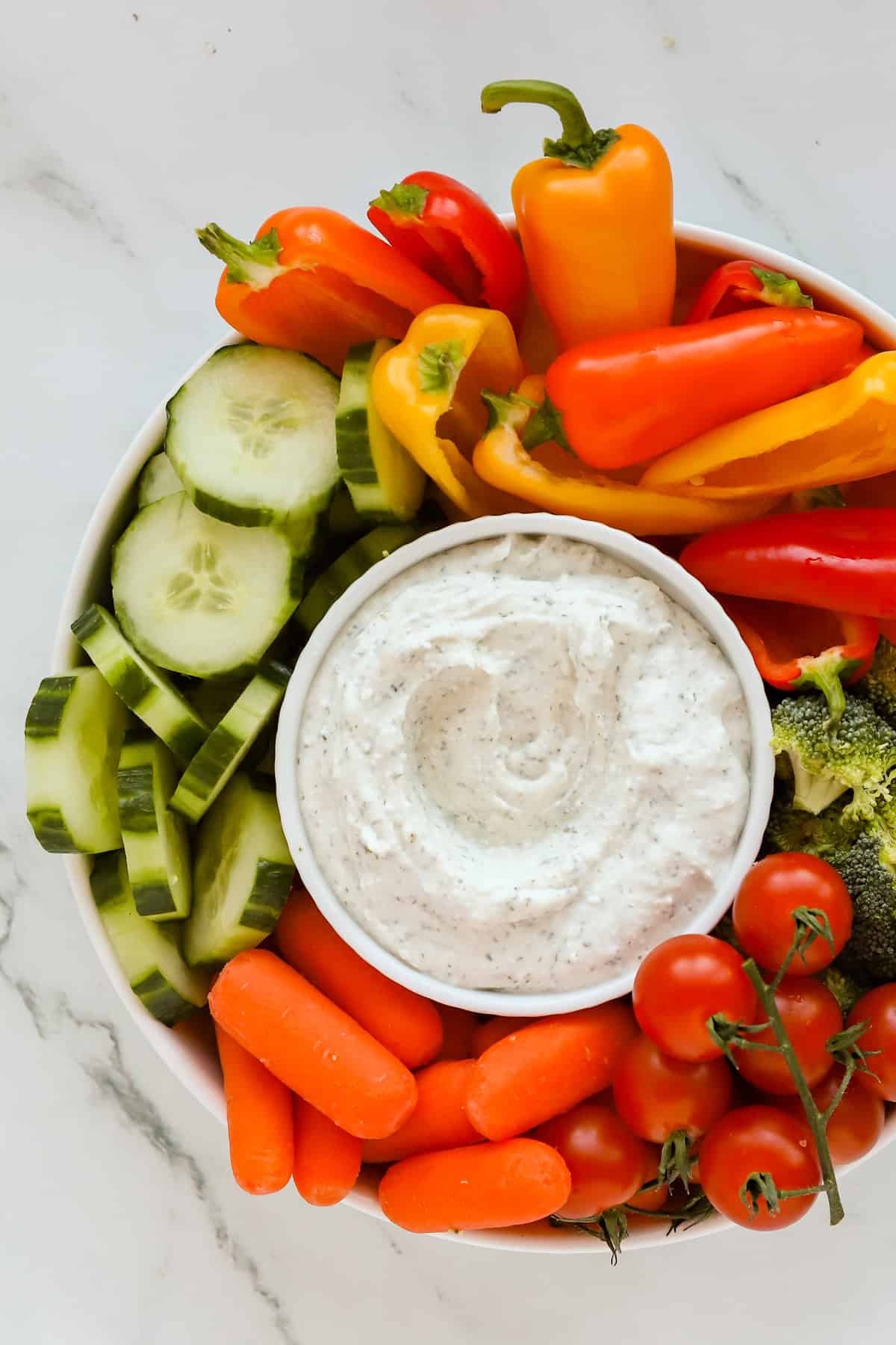 Overhead shot of round white tray of fresh vegetables with a small white bowl of dip in the middle.