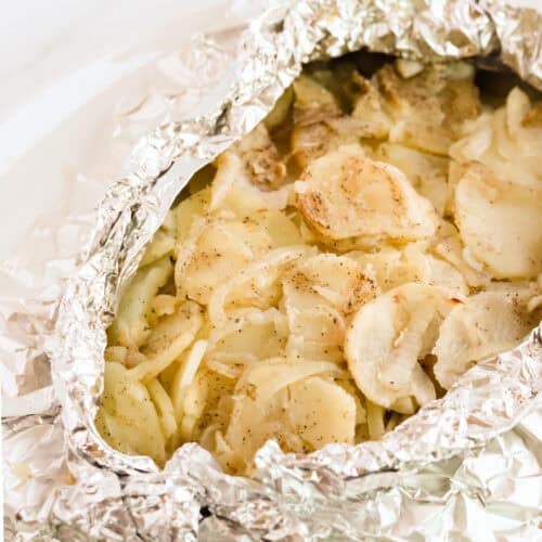 Square image of grilled potatoes in opened foil packet on a white platter.