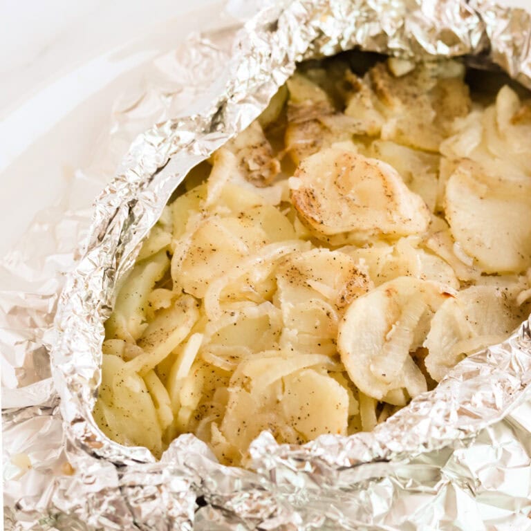 Square image of grilled potatoes in opened foil packet on a white platter.