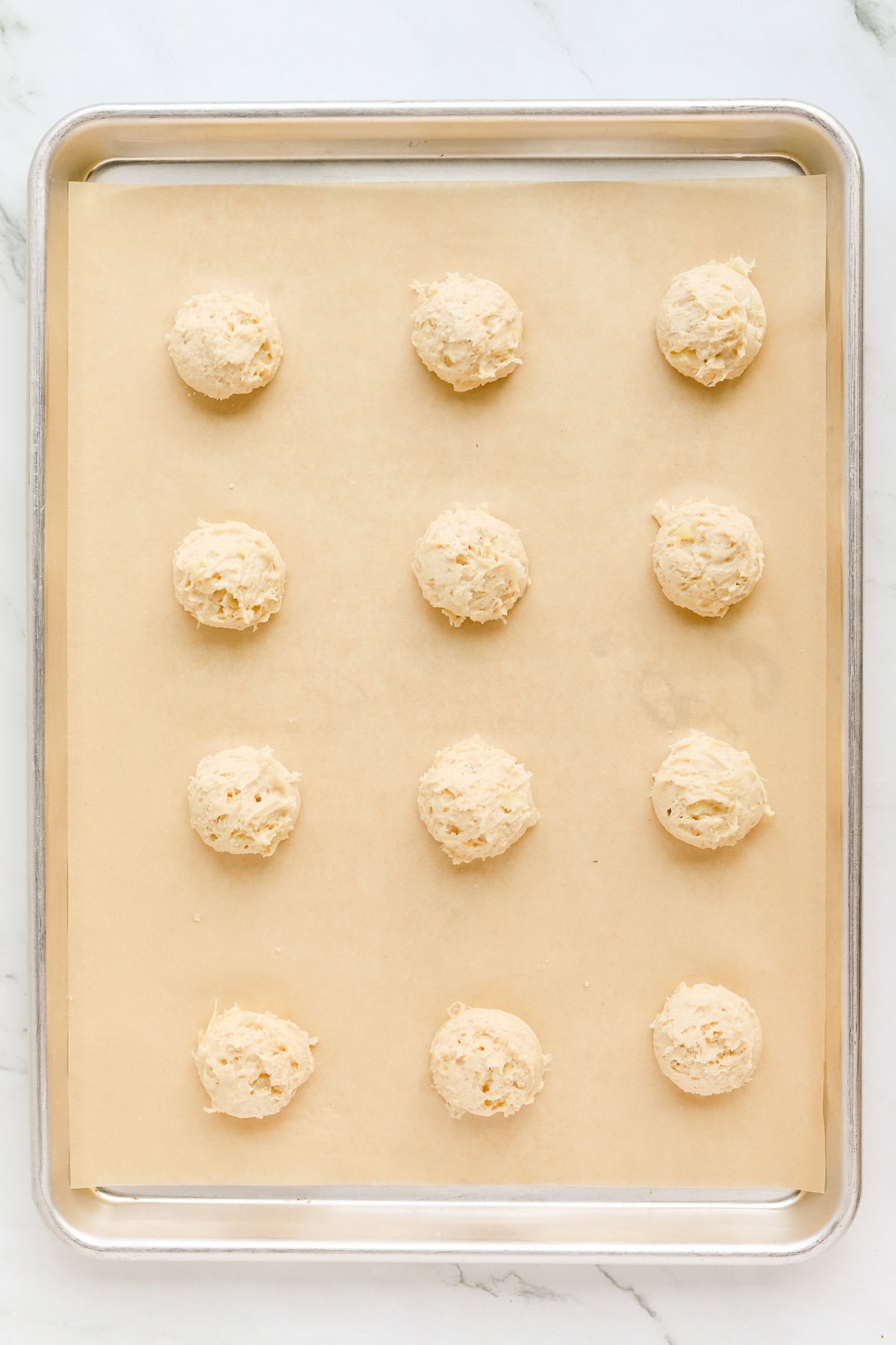 Twelve cookie dough balls evenly spaced on a parchment lined cookie sheet.