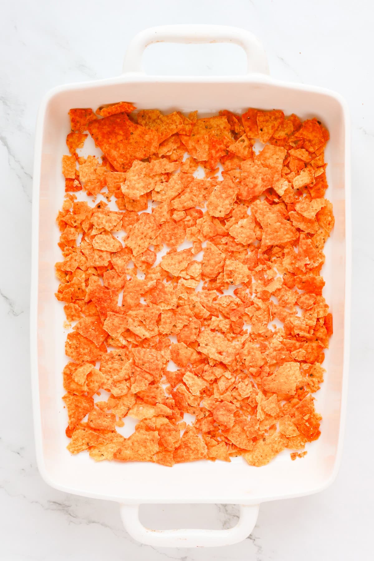 crushed nacho chips in a white 9x13 baking dish.