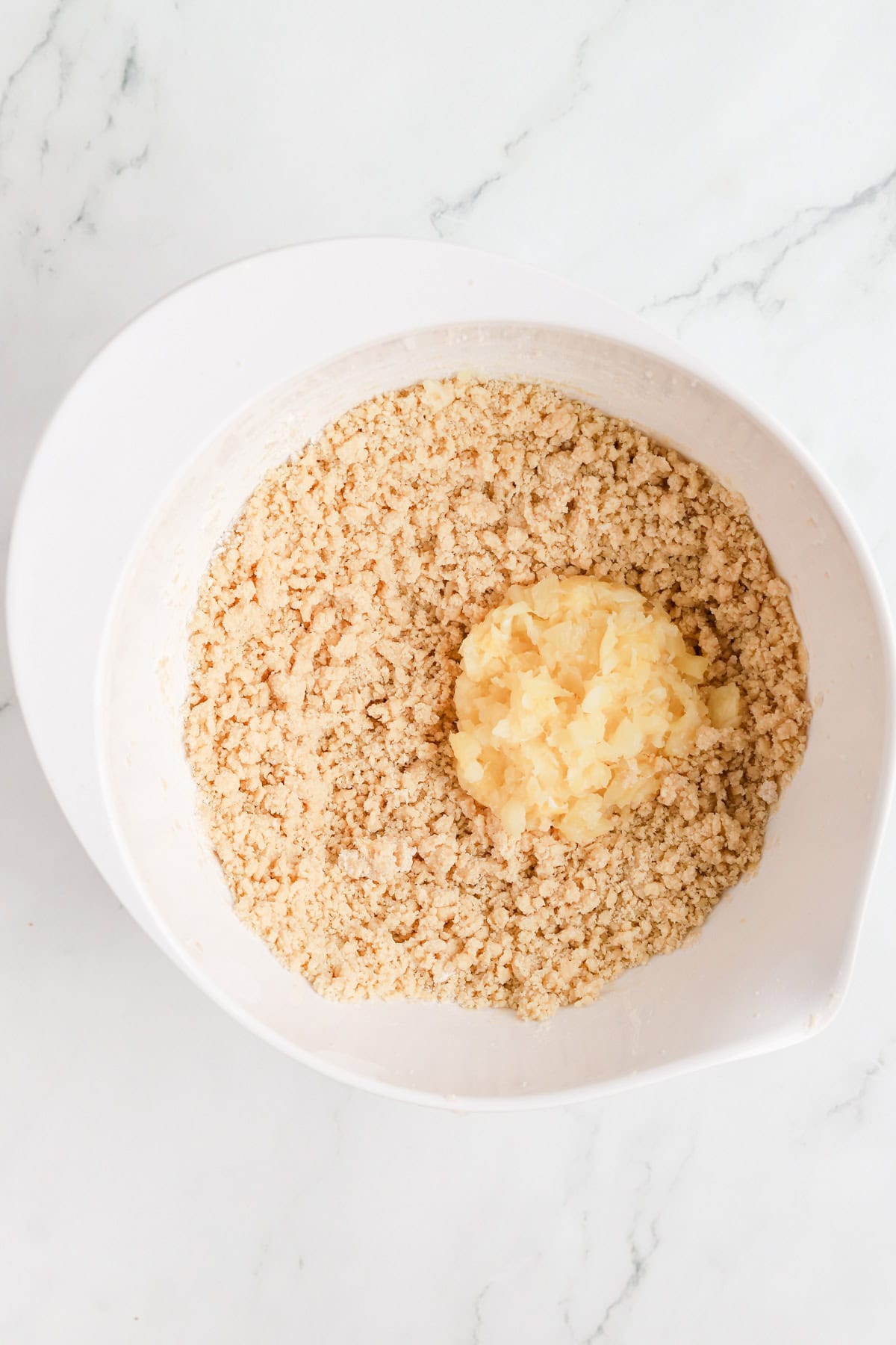 crushed pineapple on top of crumbly cookie dough in a white bowl.
