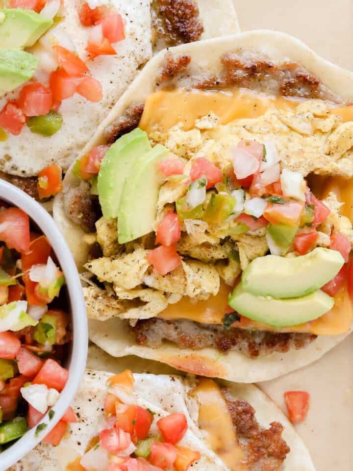 Finished breakfast tacos on a parchment lined baking sheet topped with pico de Gallo and diced avocado.