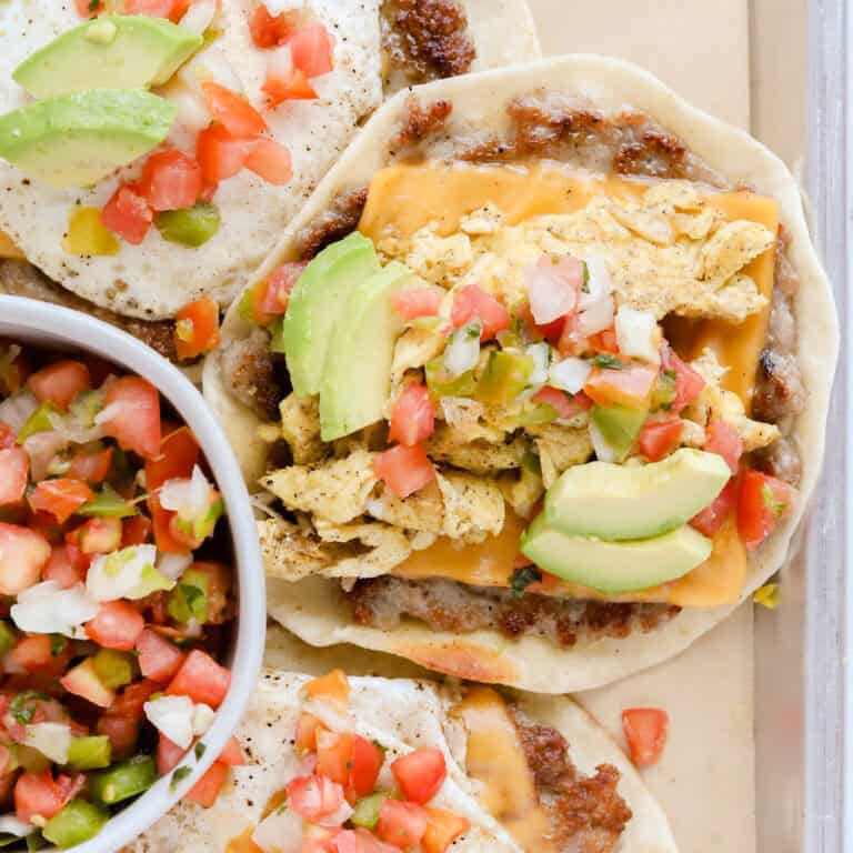 Finished breakfast tacos on a parchment lined baking sheet topped with pico de Gallo and diced avocado.