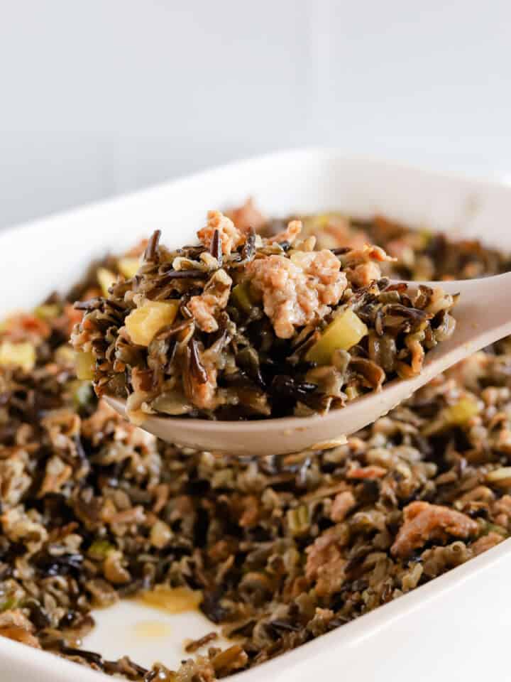 Scoop of wild rice casserole being lifted out of white baking dish.