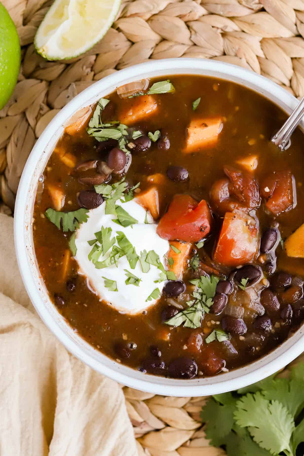 Black bean sweet potato soup garnished with sour cream and chopped cilantro in a bowl.