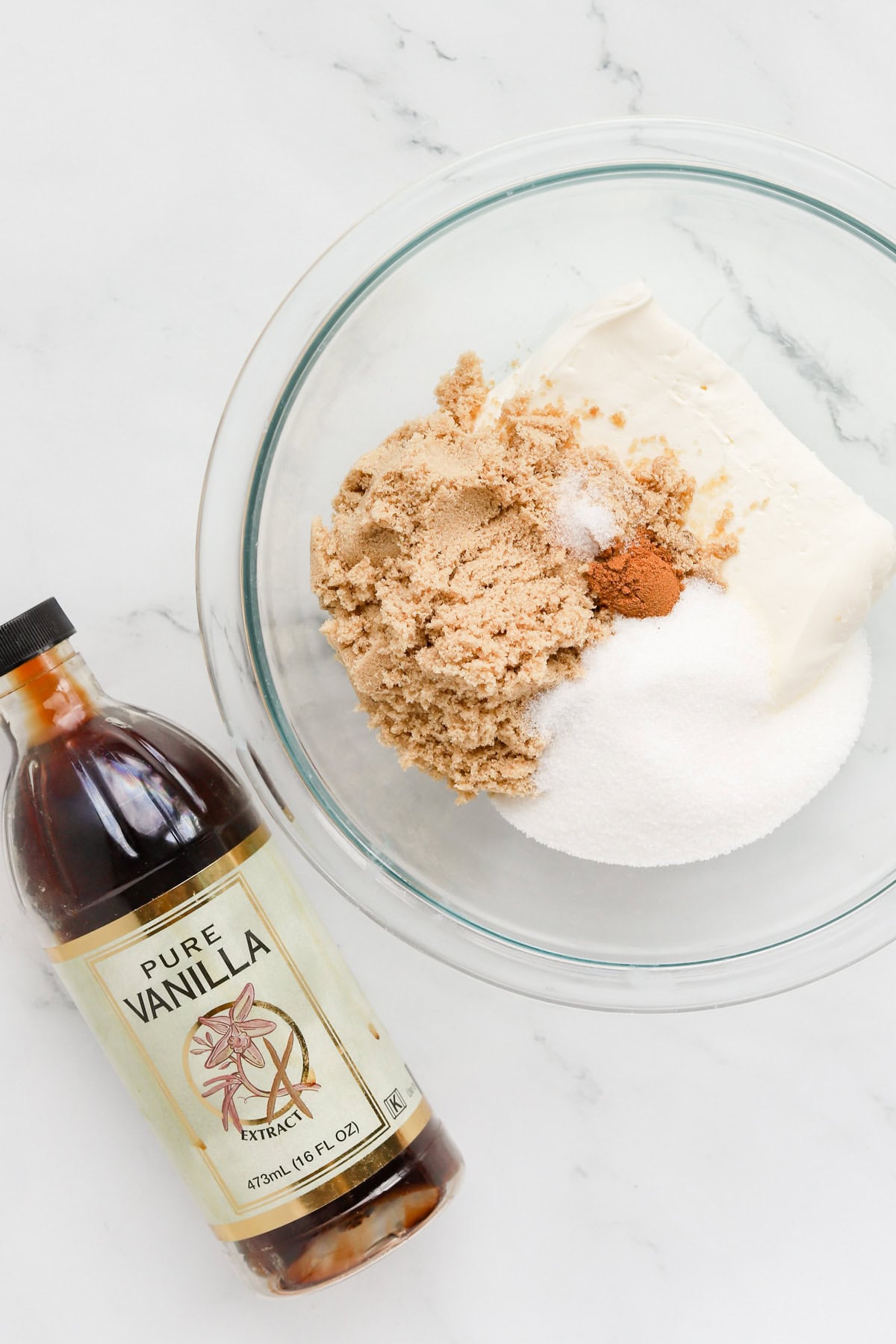 Apple dip ingredients in a glass mixing bowl and a bottle of vanilla extract laying next to it.