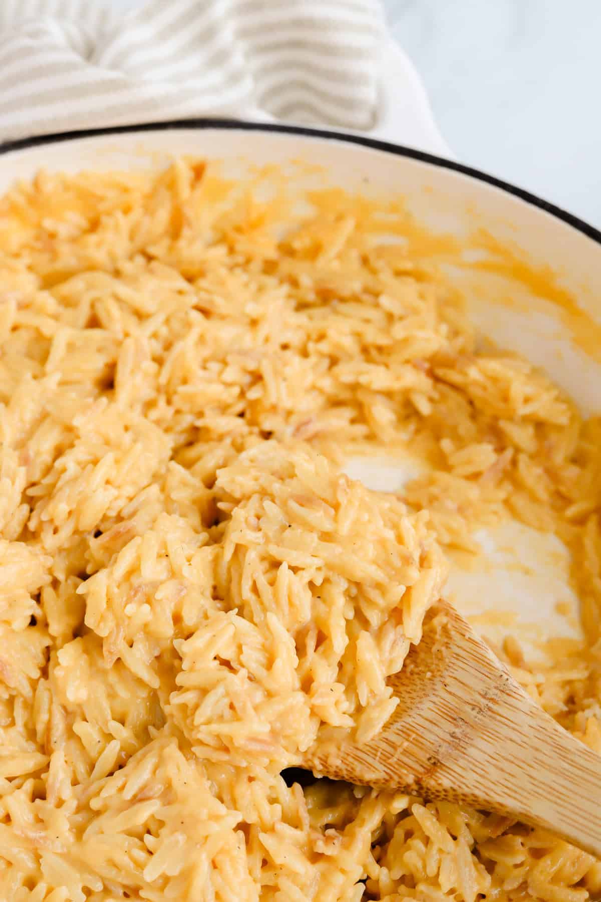 Finished cheesy orzo in skillet with wooden spoon.