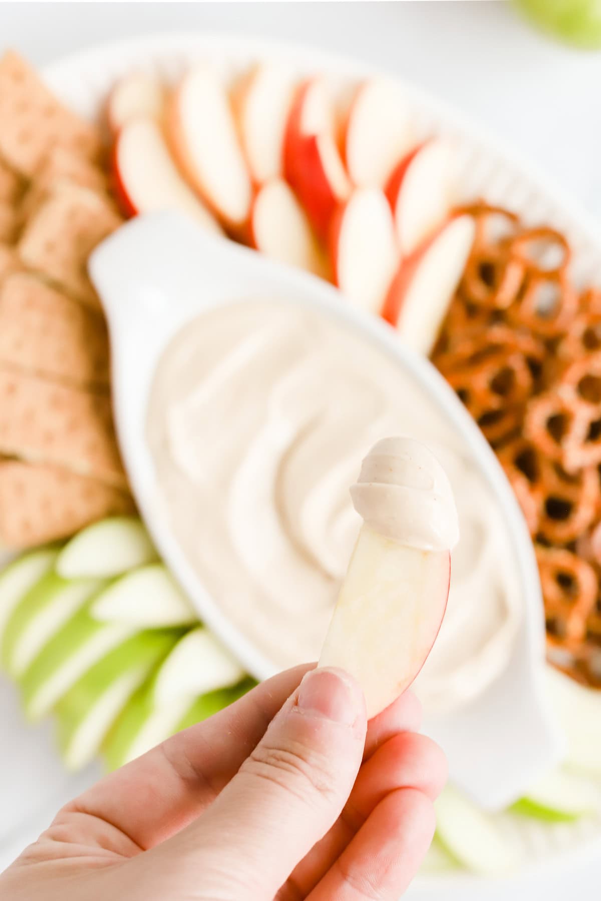 Close up on hand dipped apple slice with dip over platter.
