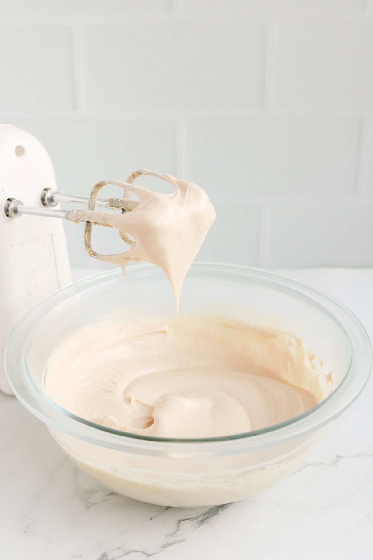 Hand mixer beaters full of dip resting over glass bowl full of dip.