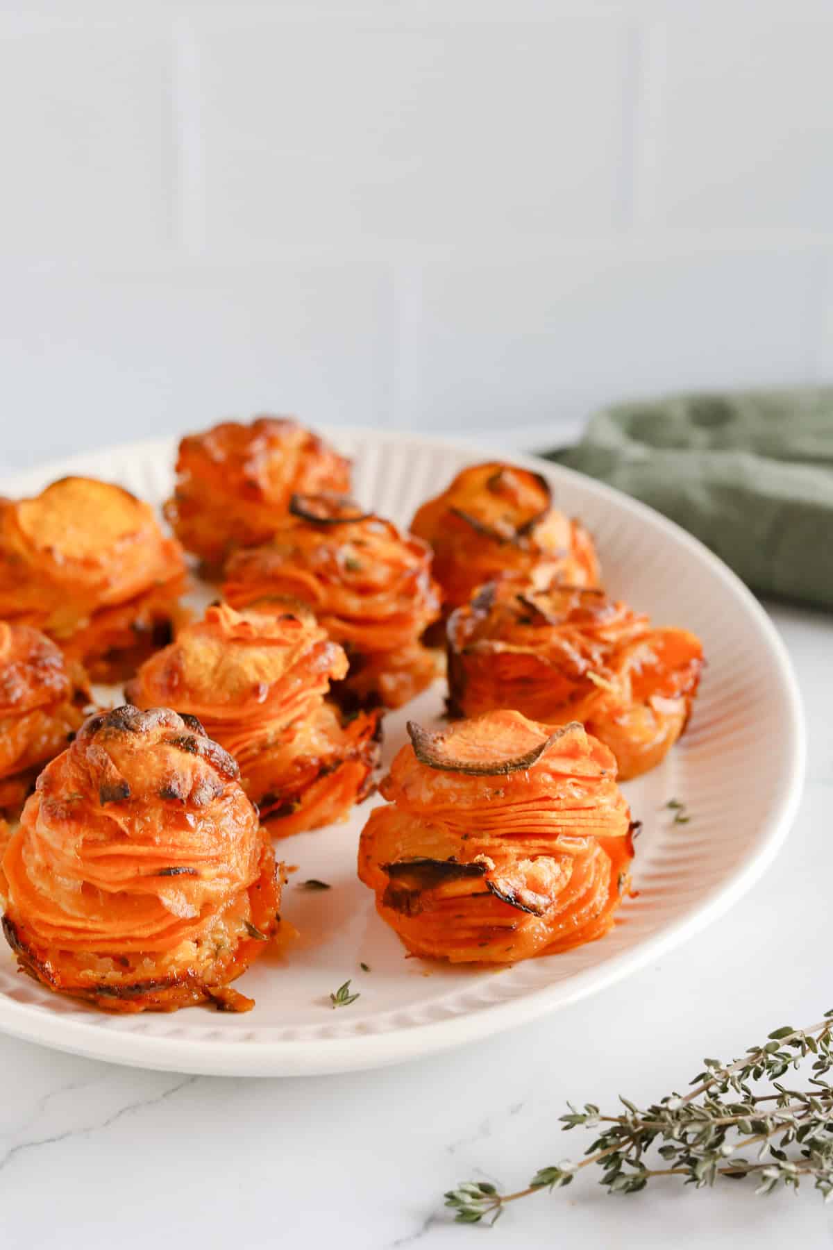 Sweet potato stacks displayed nicely on a white oval platter and garnished with thyme.