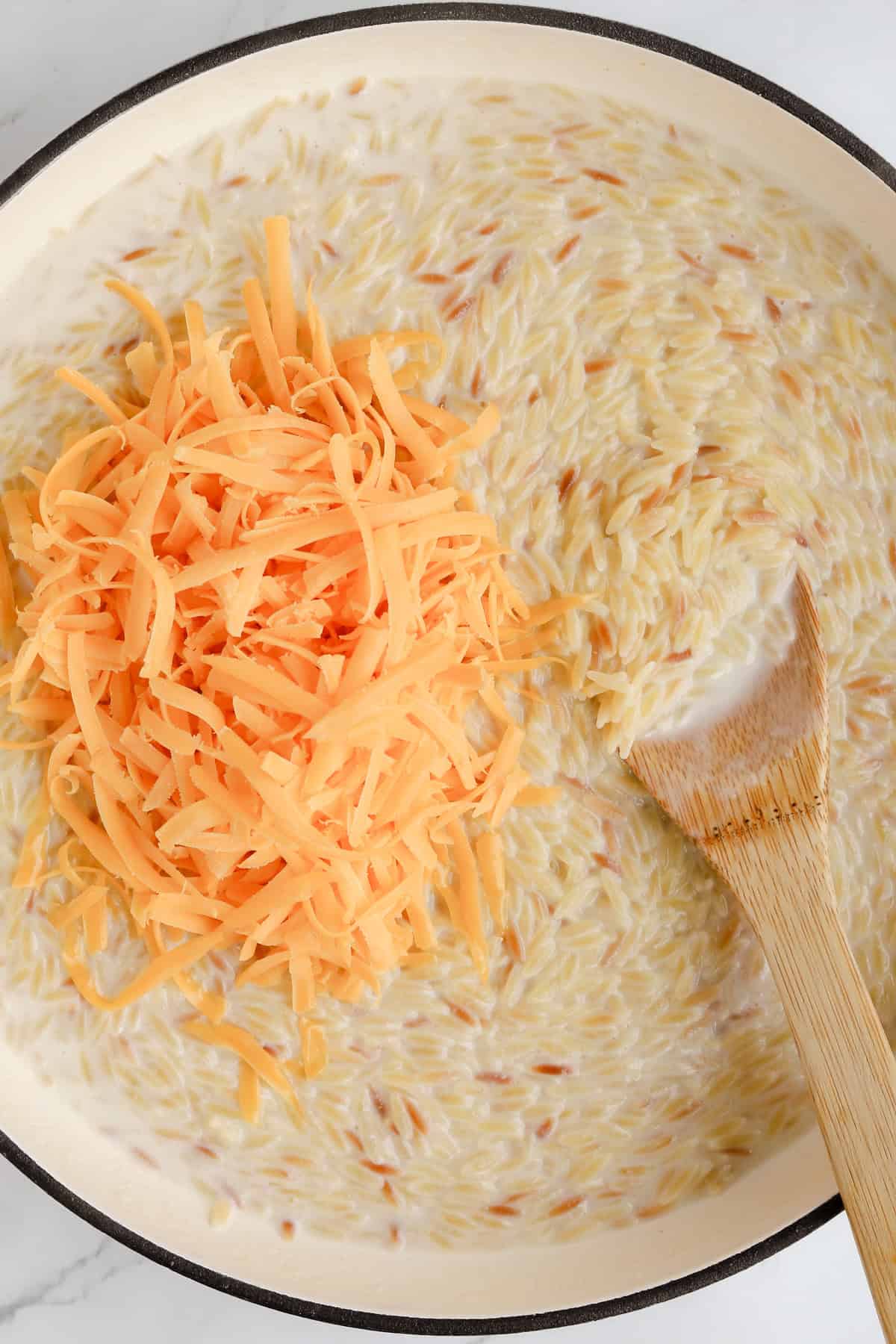 Shredded cheddar cheese added on top of cooked orzo to create creamy cheese sauce.