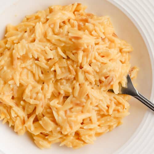 Cheesy orzo served in a white shallow bowl with a fork.
