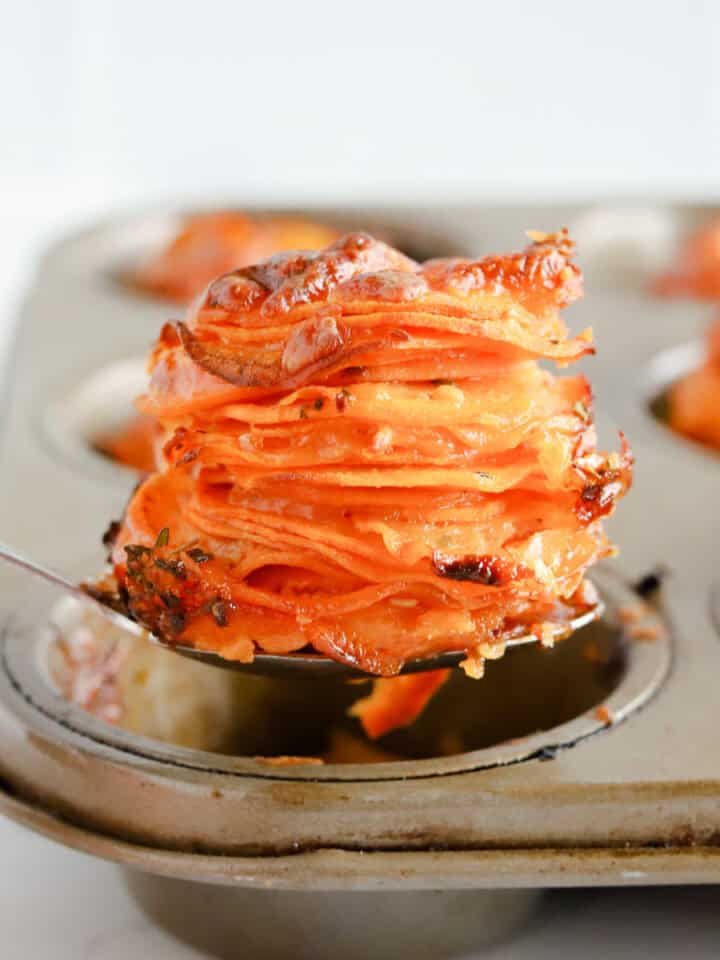 Square photo of a spoon lifting a potato stack out of the muffin tin.