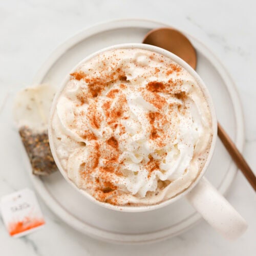 Overhead shot of chocolate chai latte with whipped cream and cinnamon on a saucer with spoon and a tea bag.