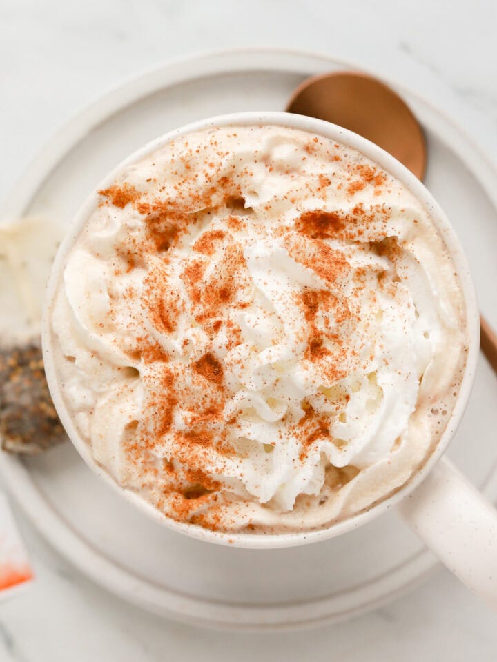 Overhead shot of chocolate chai latte with whipped cream and cinnamon on a saucer with spoon and a tea bag.