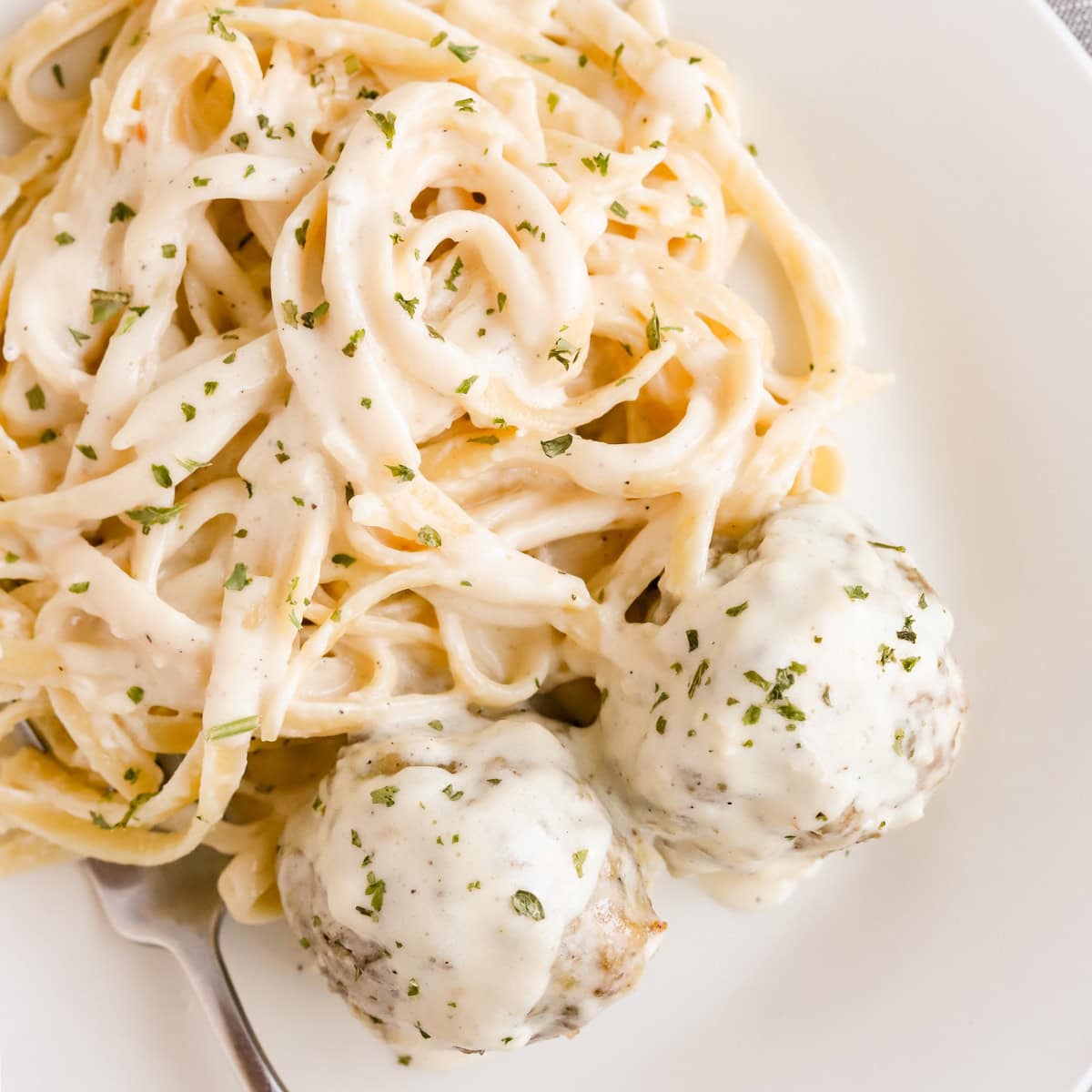 Square photo of fettuccine alfredo with meatballs.