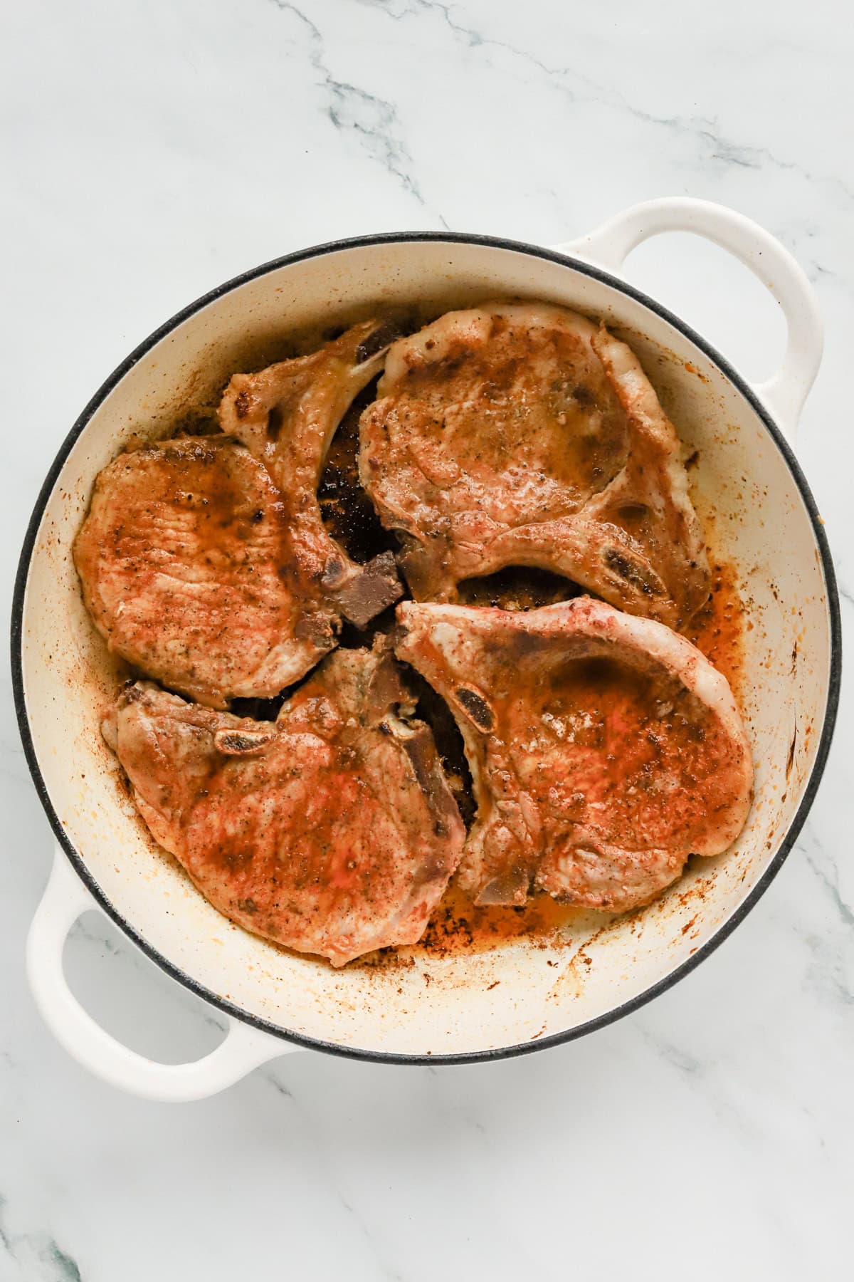 Seared pork chops in white ceramic skillet.