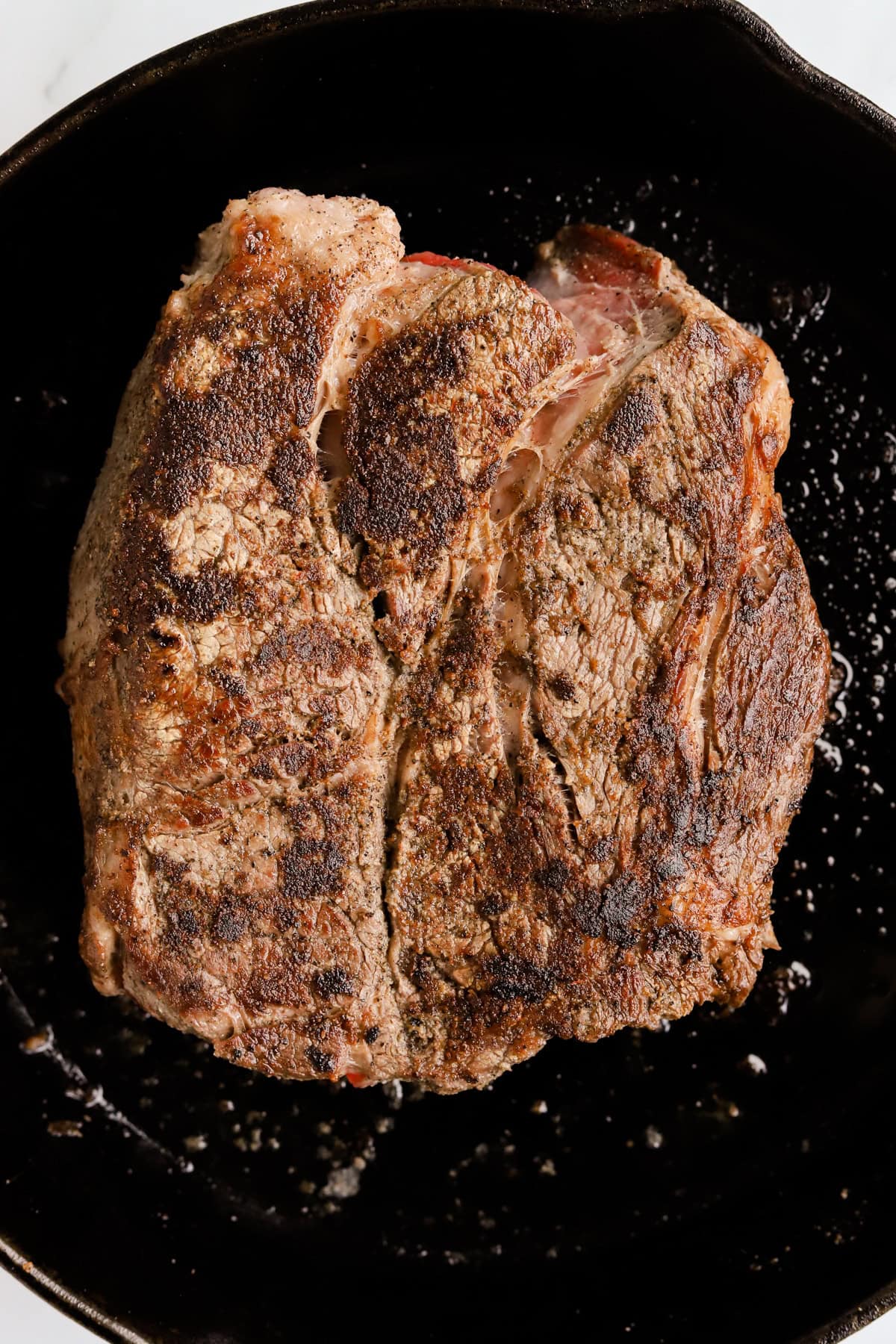 Chuck roast seared on both sides in a cast iron skillet.