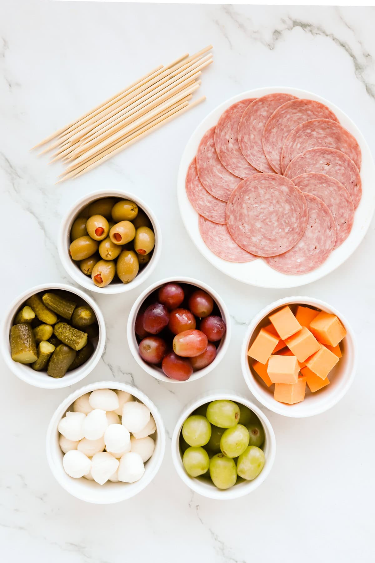 Charcuterie ingredients in bowls and on plates on a marble countertop.