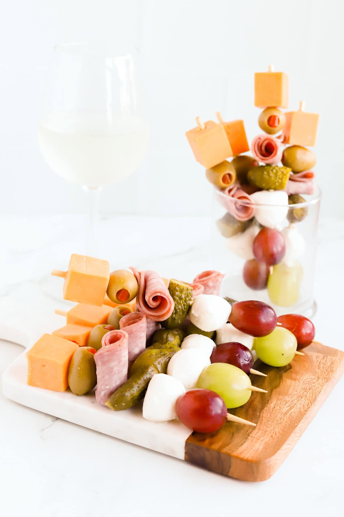 Charcuterie skewers displayed on a board and standing up in a clear glass.