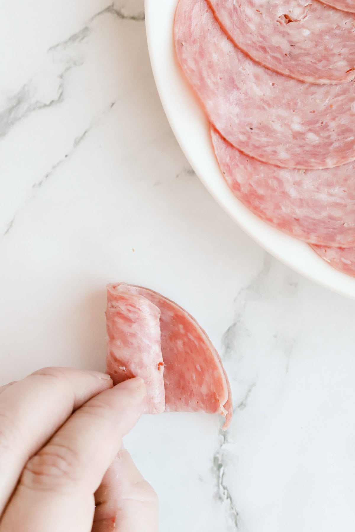 Hand rolling a salami rose on marble countertop.