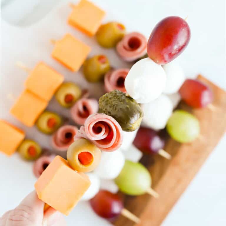 Hand holding a charcuterie skewer above a board of skewers