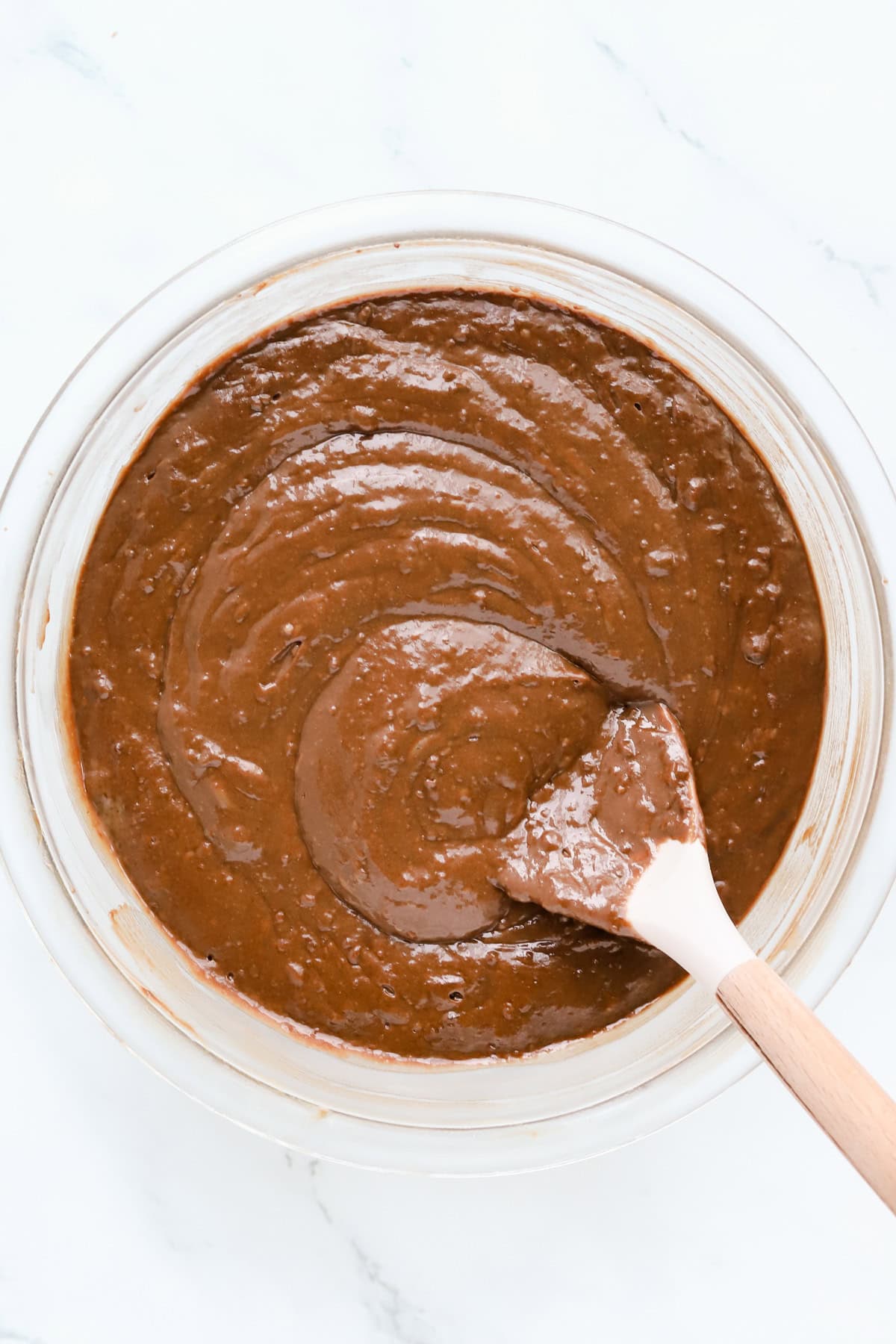 Chocolate cake batter in a glass bowl with a rubber spatula.