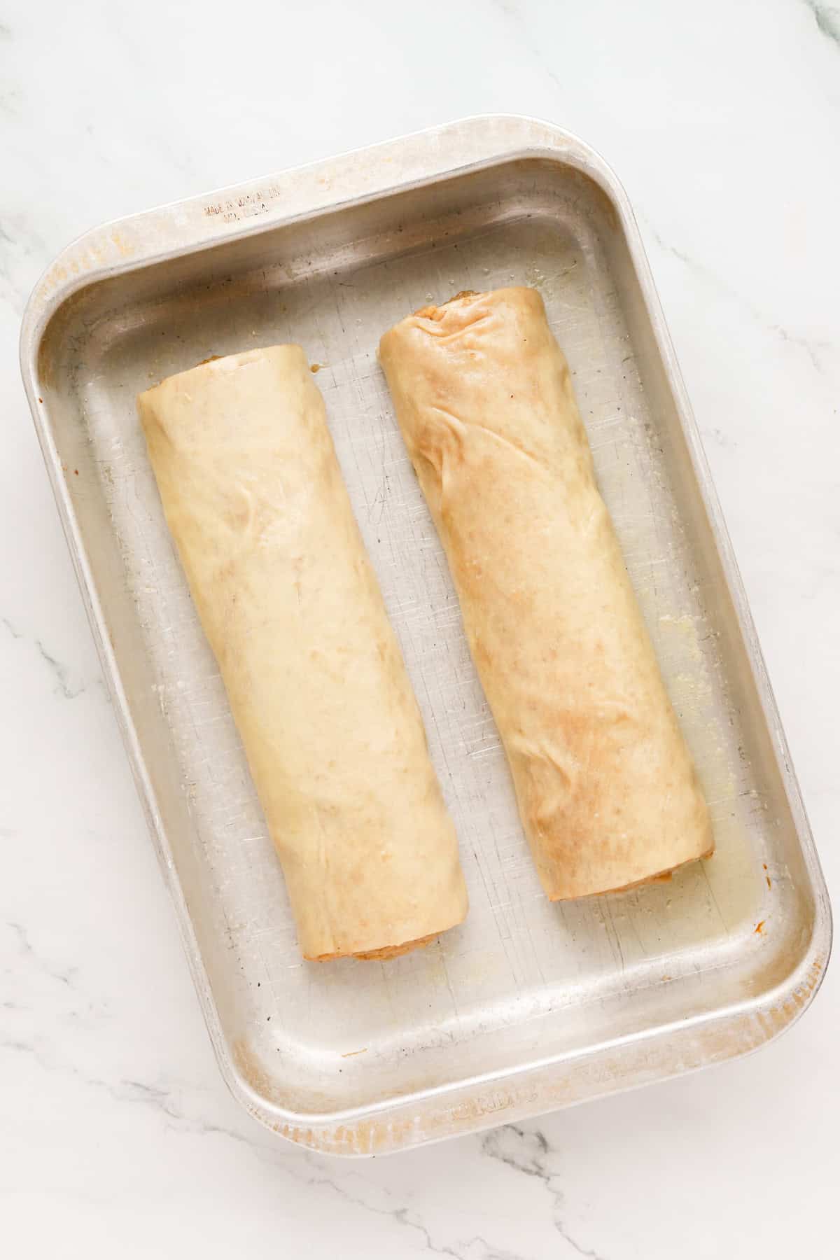 Two potica loaves rolled in melted butter in a metal 9x13 baking pan.