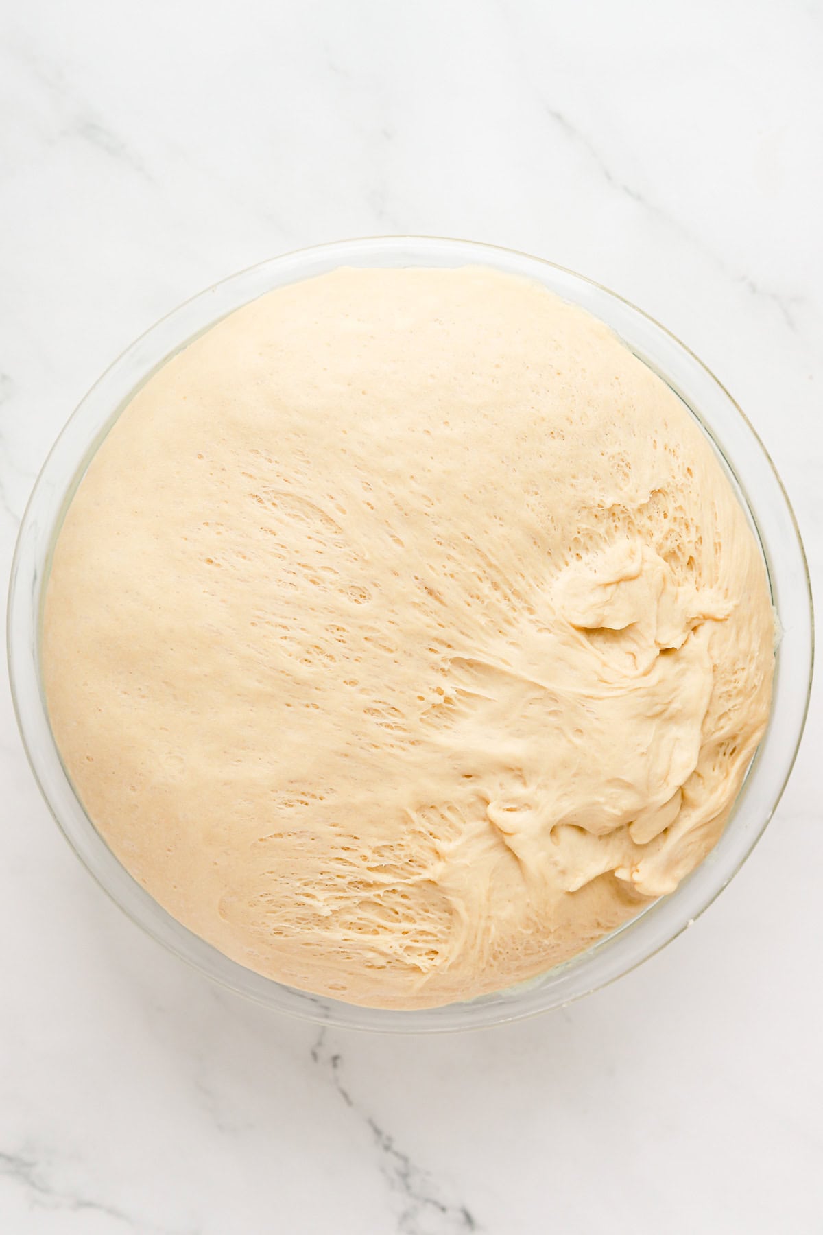 Proofed yeast dough in a clear glass bowl.