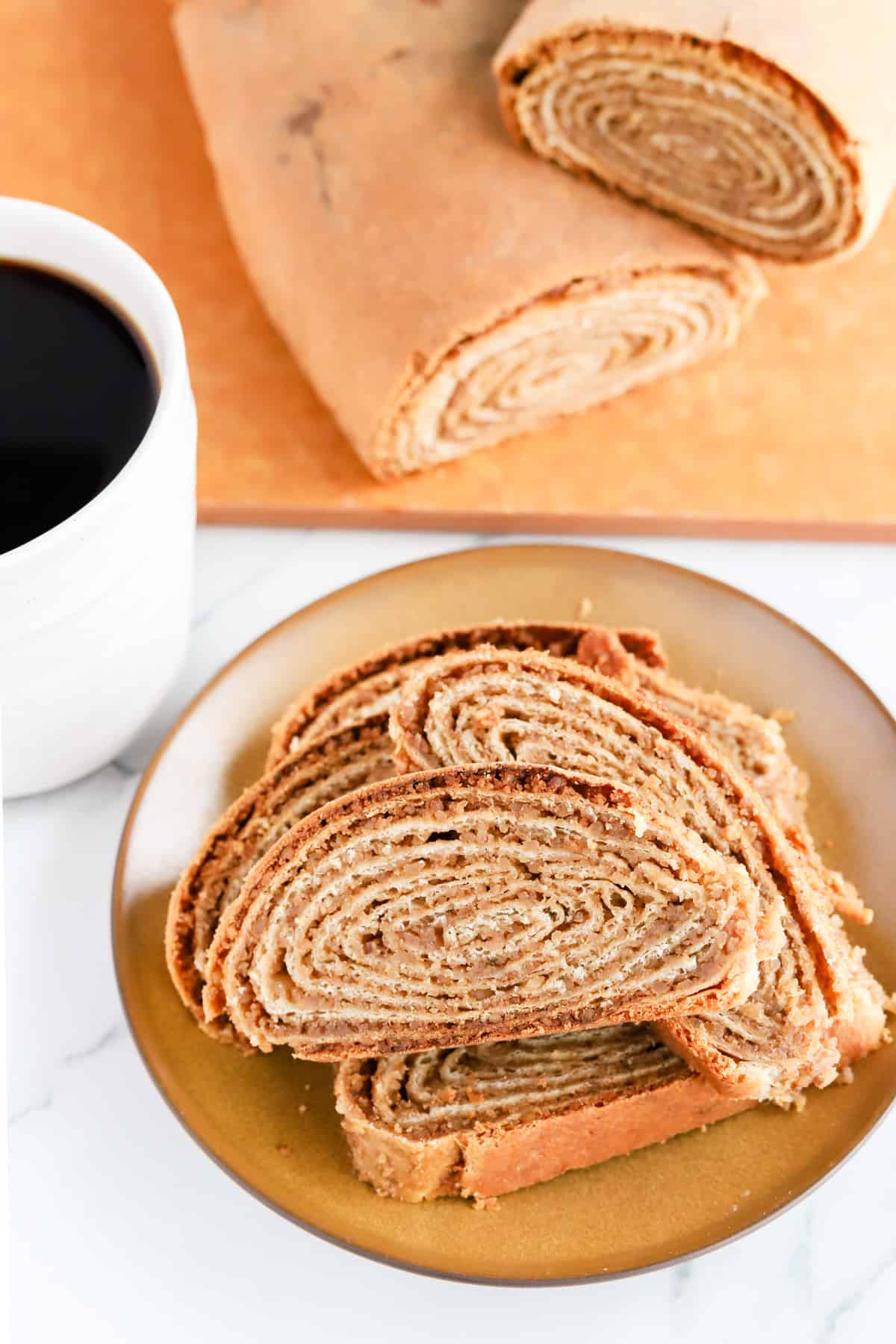 Sliced potica on a plate with a cup of coffee and loaves on a wood cutting board.