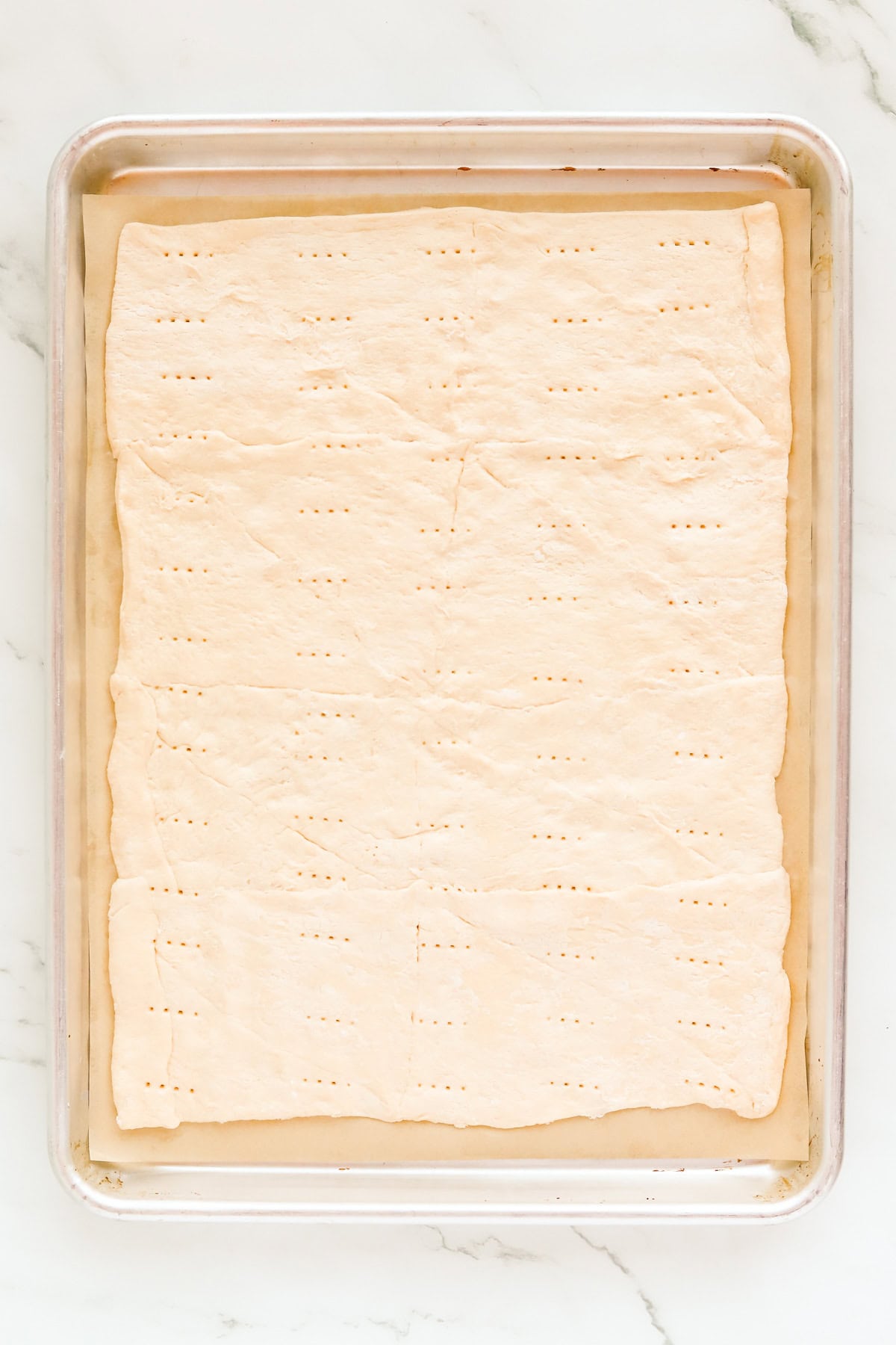 Two crescent roll tubes pressed into a rectangle on a parchment lined baking sheet with fork holes throughout.