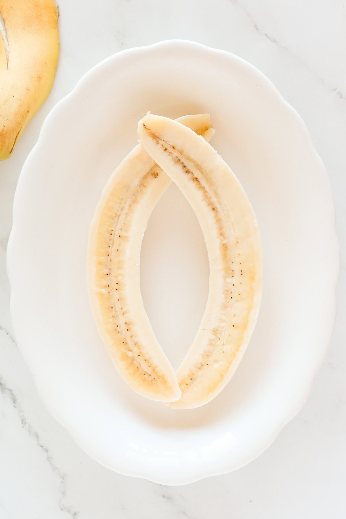 Banana split in half lengthwise on a white plate.