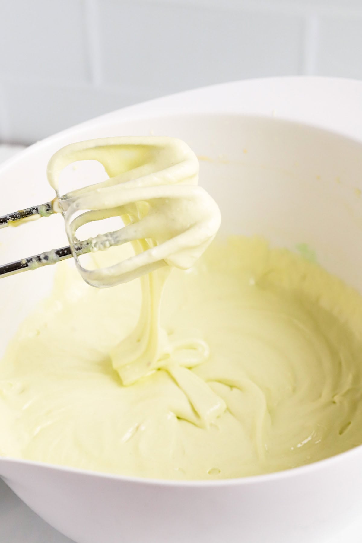 Cake batter in a white bowl with hand mixer beaters drizzling batter into the bowl.