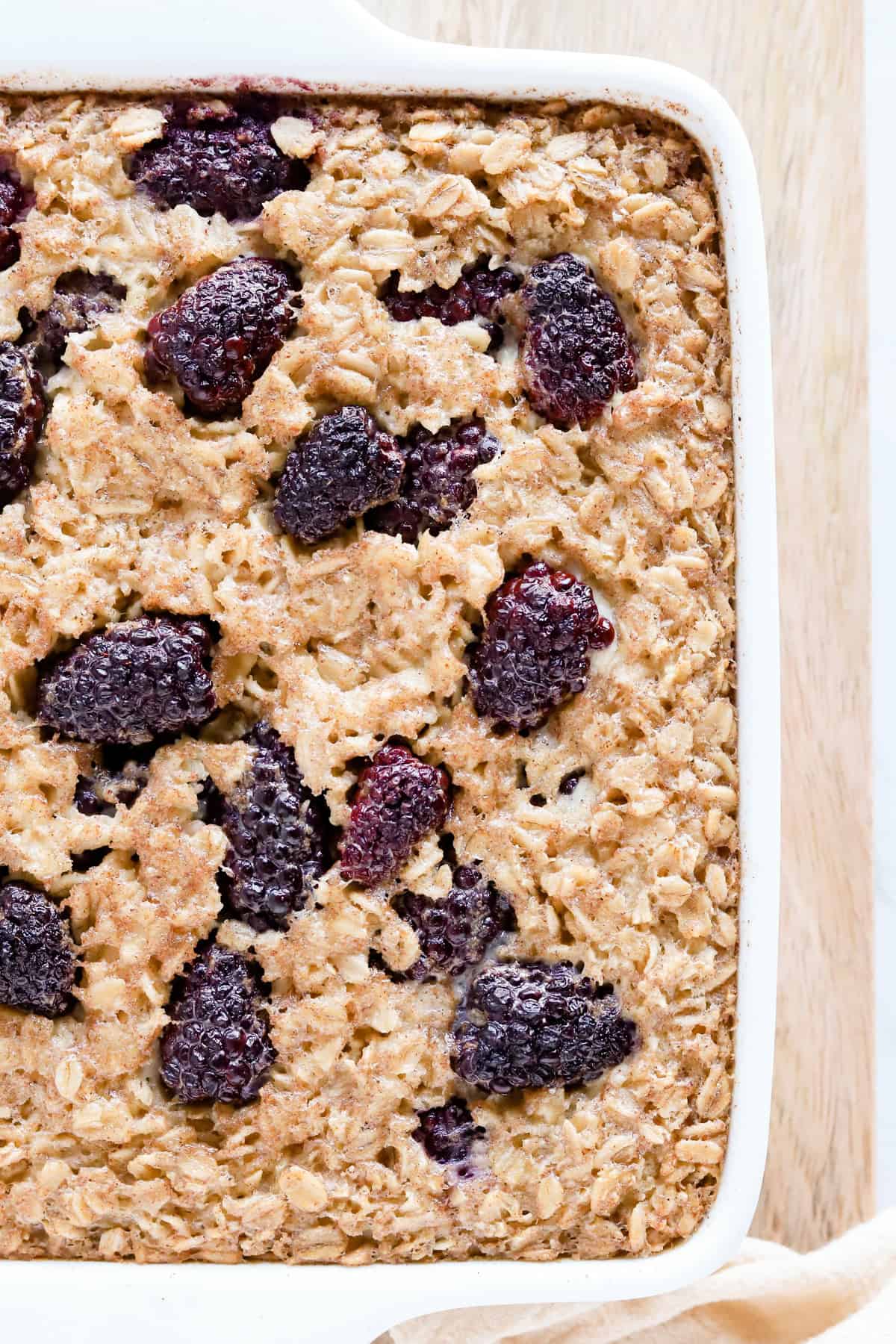 Baked blackberry oatmeal in a white square baking dish on a wooden board.