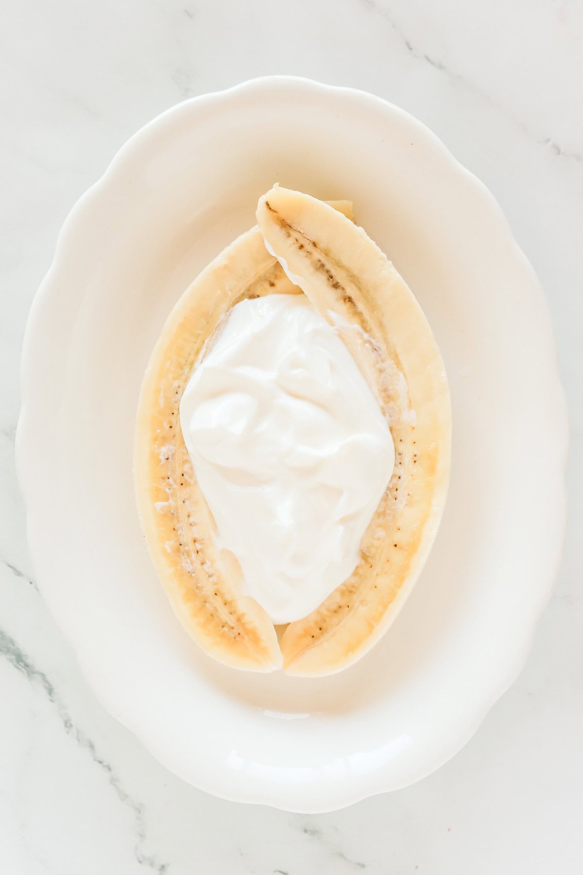 Vanilla yogurt in middle of split banana pieces on a white plate.
