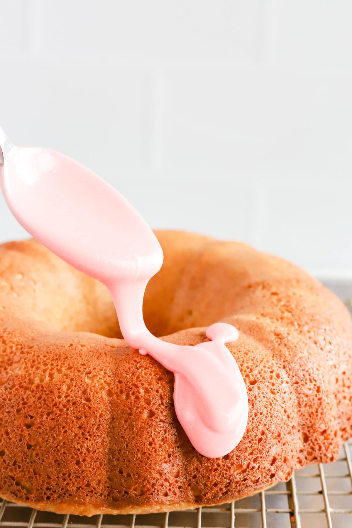 Spoon drizzling pink cherry glaze over pistachio bundt cake.
